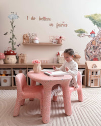 Child sitting at a pink table in a playroom with fairy-themed decor.