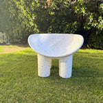 Concrete chair on grass with greenery in the background