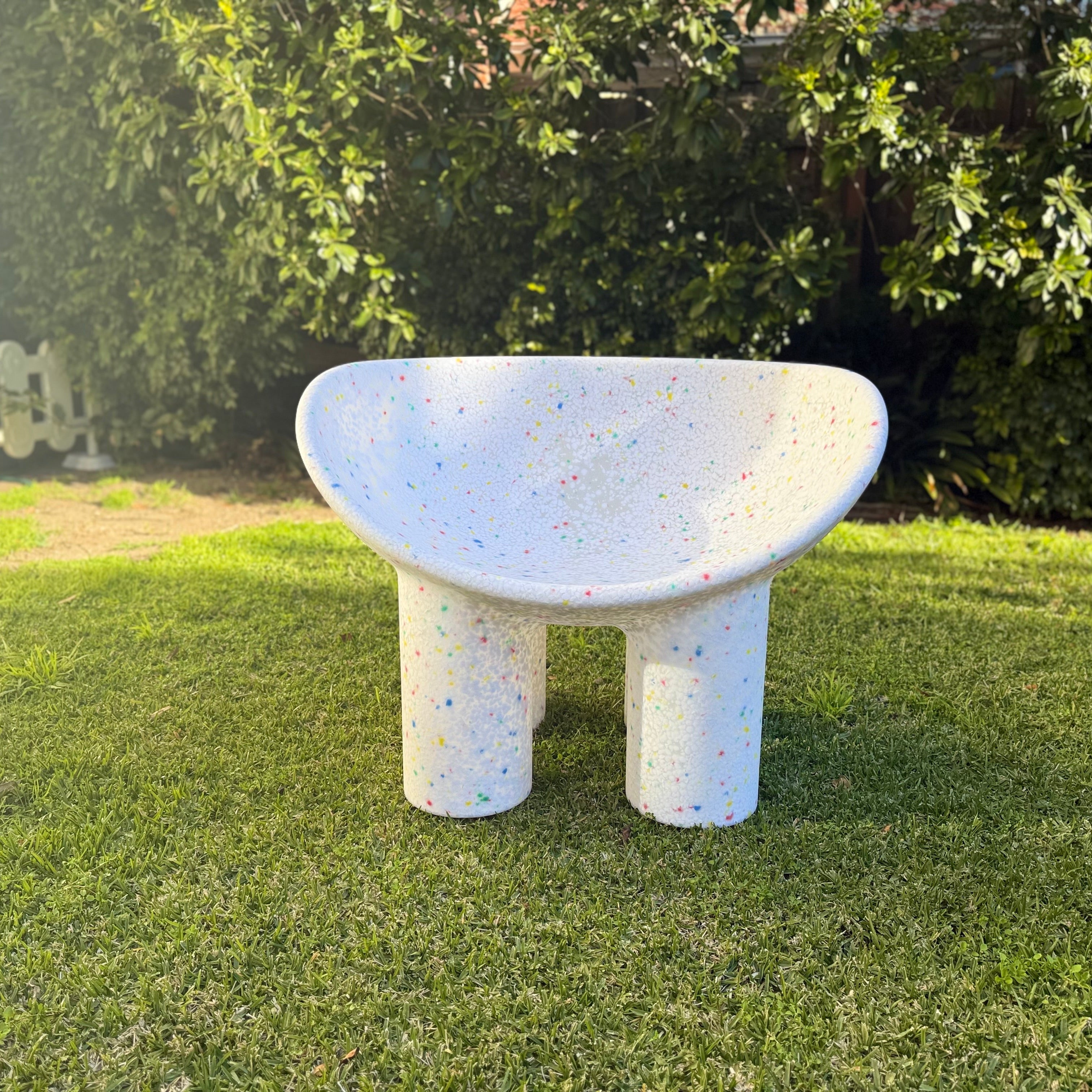 Concrete chair on grass with greenery in the background