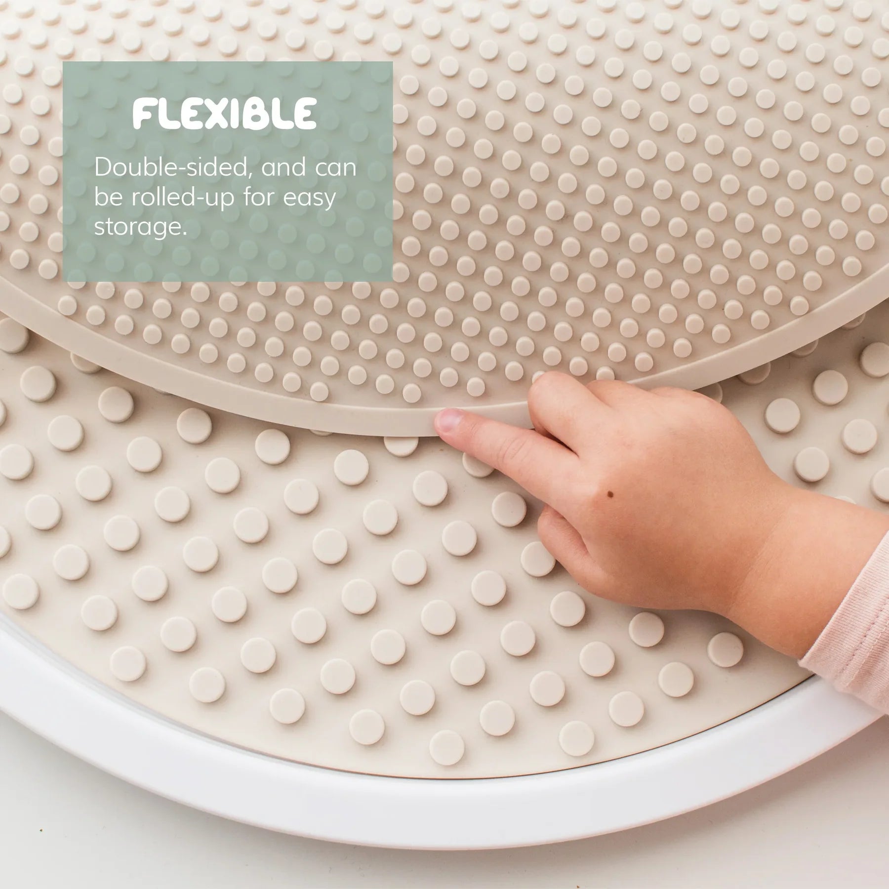 Round flexible mat with textured surface and a hand touching it, on a light background.