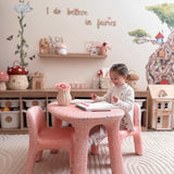 Child sitting at a pink table in a playroom with fairy-themed decor.