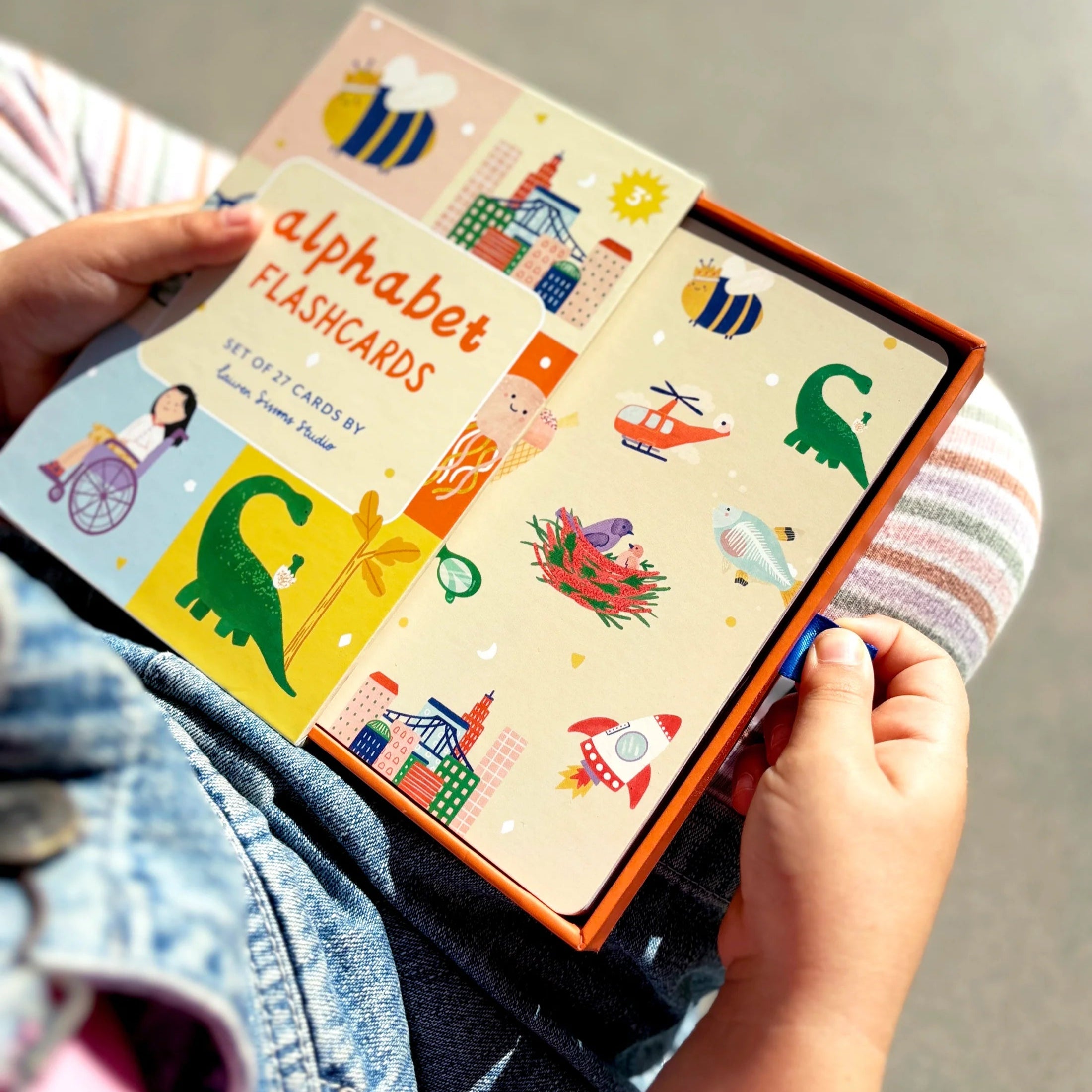 Child holding alphabet flashcards with colorful illustrations on a neutral background