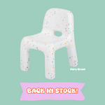 White chair-shaped pillow with colorful sprinkles on a light green background, featuring the brand 'Fairy Bread'.