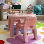 Pink children's table and chair set with toys on a colorful rug in a playroom.