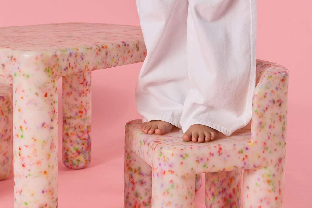 Children's legs on a colorful stool against a pink background