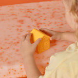 Child playing with a yellow toy house on an orange and pink patterned surface