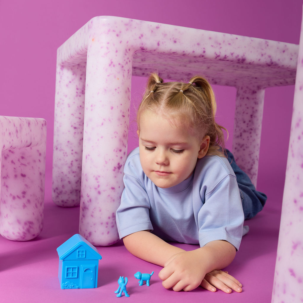 Child playing with toys on a pink floor with pink and white geometric structures in the background.