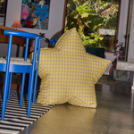 Yellow checkered pillow on a chair in a room with a blue chair and striped rug.