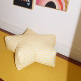 Star-shaped cushion on a yellow floor with framed artwork on the wall.