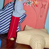 Child in red pants standing next to a bed with yellow striped bedding, against a pink wall with decorative elements.