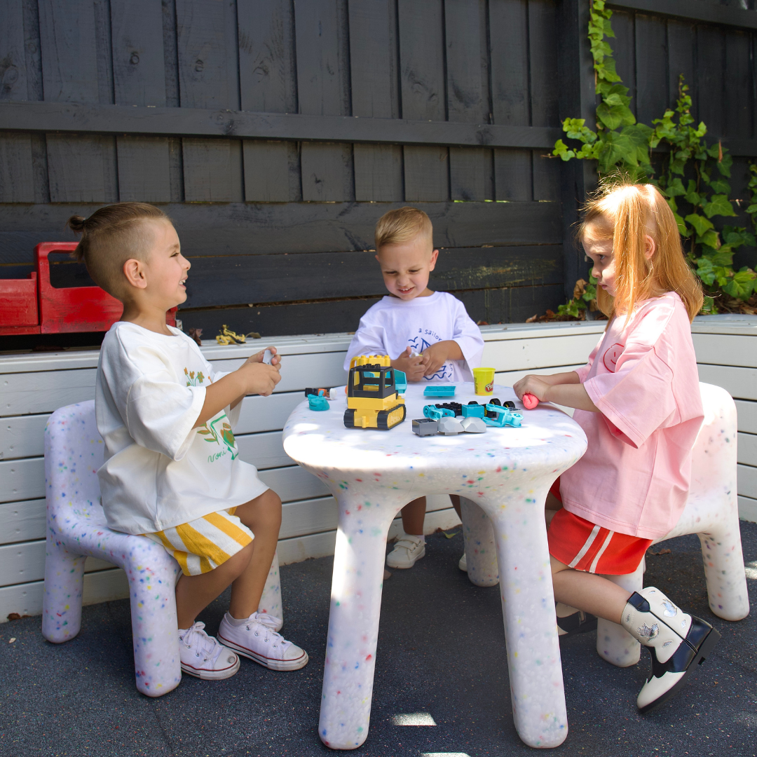 Three children playing with toys at a small table outdoors.