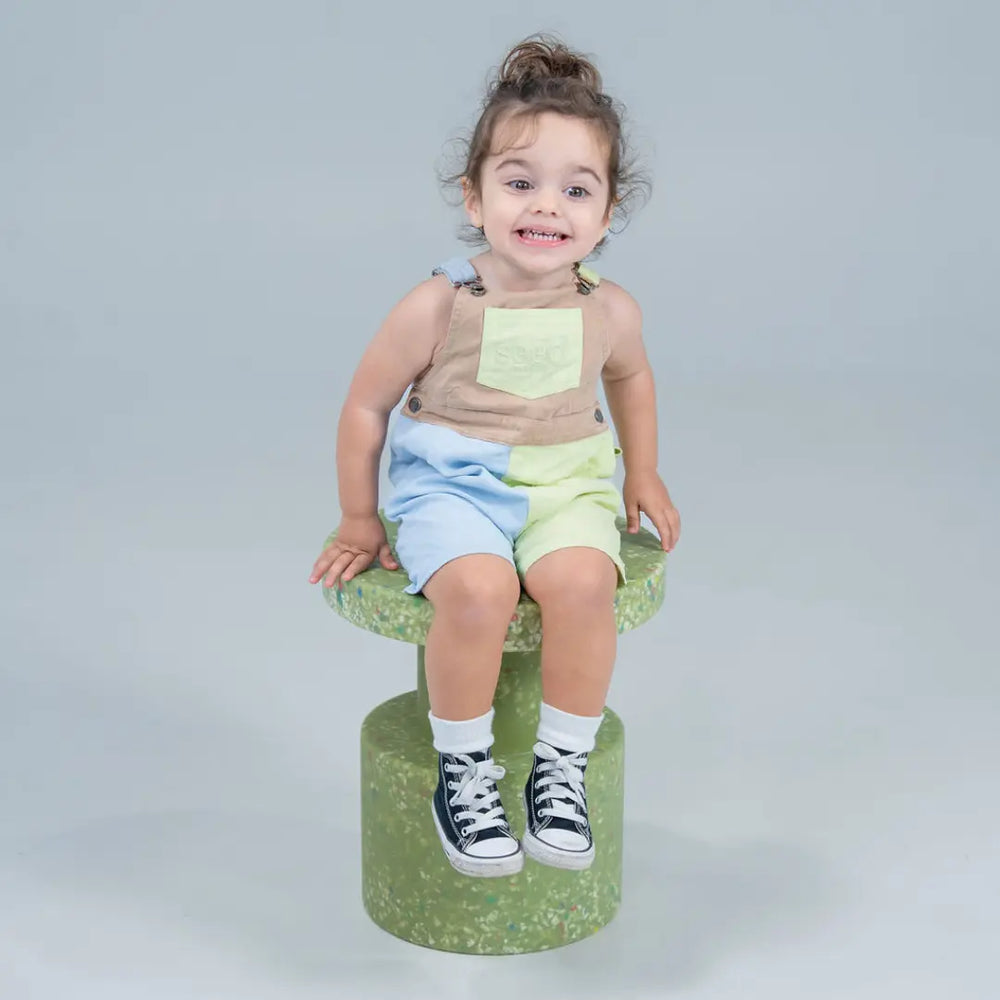 Child sitting on a green stool against a gray background