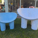 Two blue and white speckled chairs on grass with a glass building in the background.