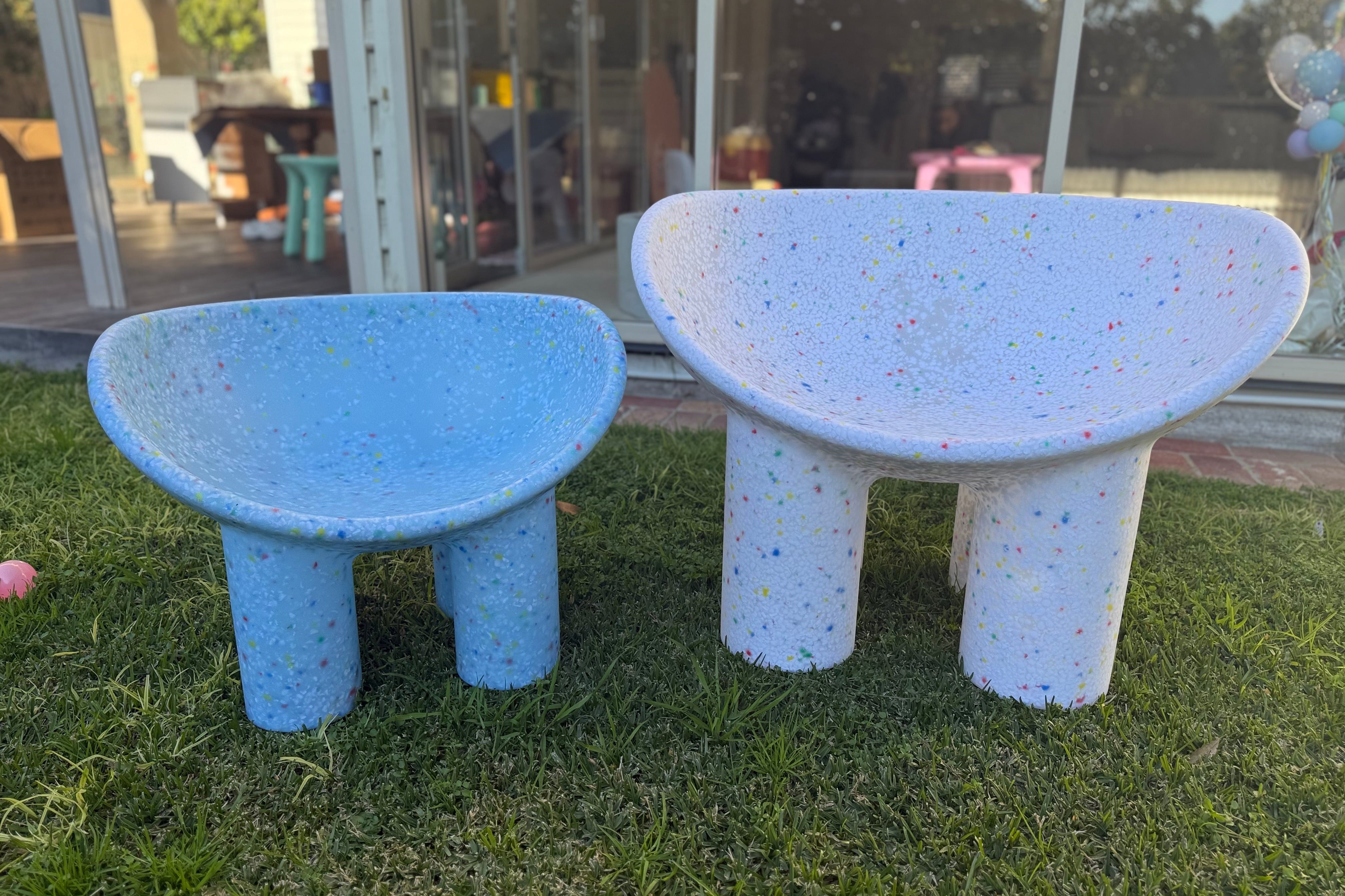 Two blue and white speckled chairs on grass with a glass building in the background.