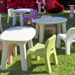 Children's play area with colorful chairs and tables on grass, decorated with balloons and 'ONE' letter set.