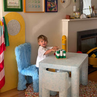 Child playing at a table with toys in a room decorated with colorful frames and a yellow clock.