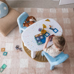 Child playing with toys on a small round table in a room with a carpeted floor.