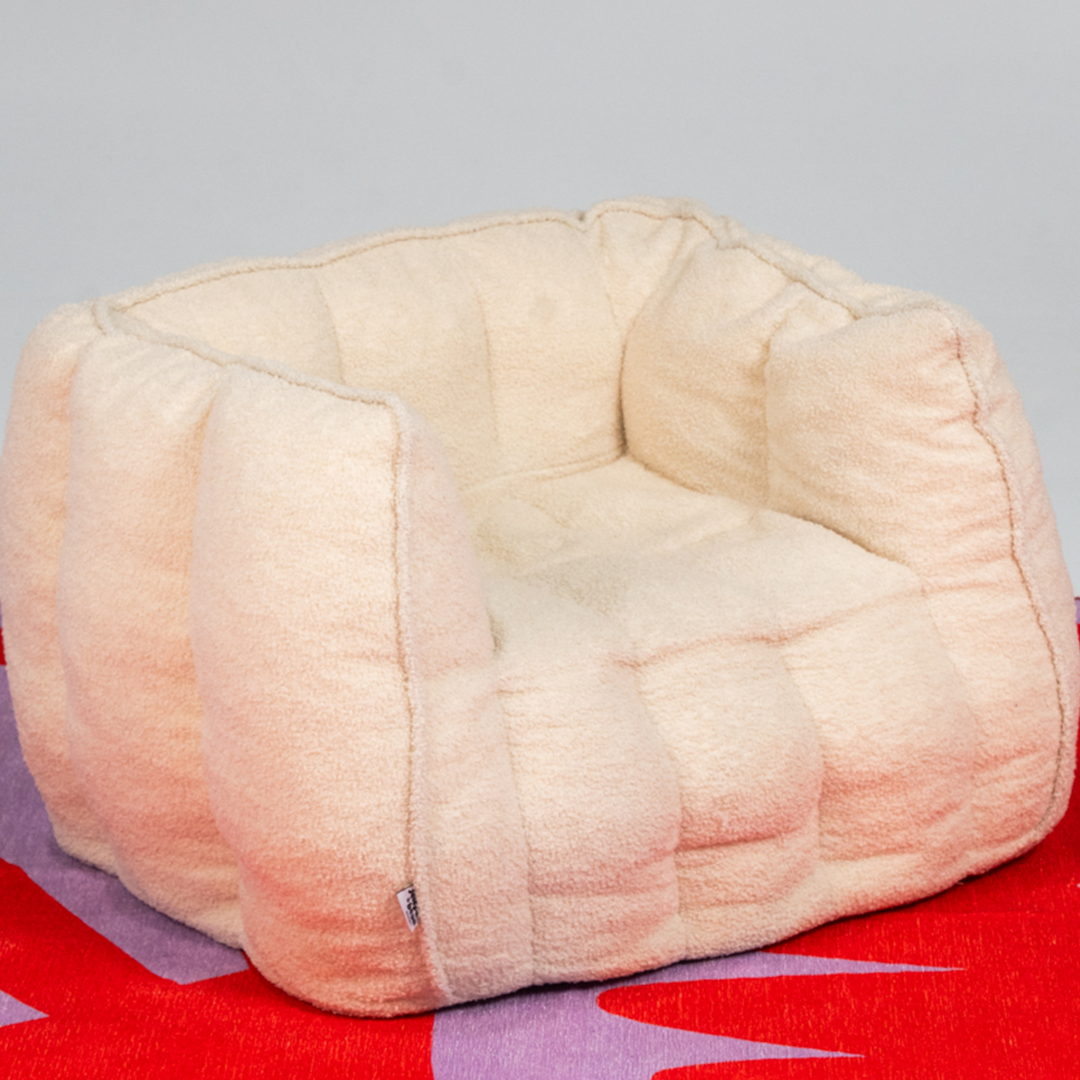 Beige Toddler couch seat on a colorful mat with a plain background