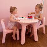 Two young girls sitting at a pink table with chairs in a room with pink walls.