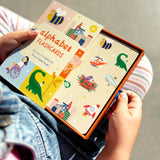 Child holding alphabet flashcards with colorful illustrations on a neutral background