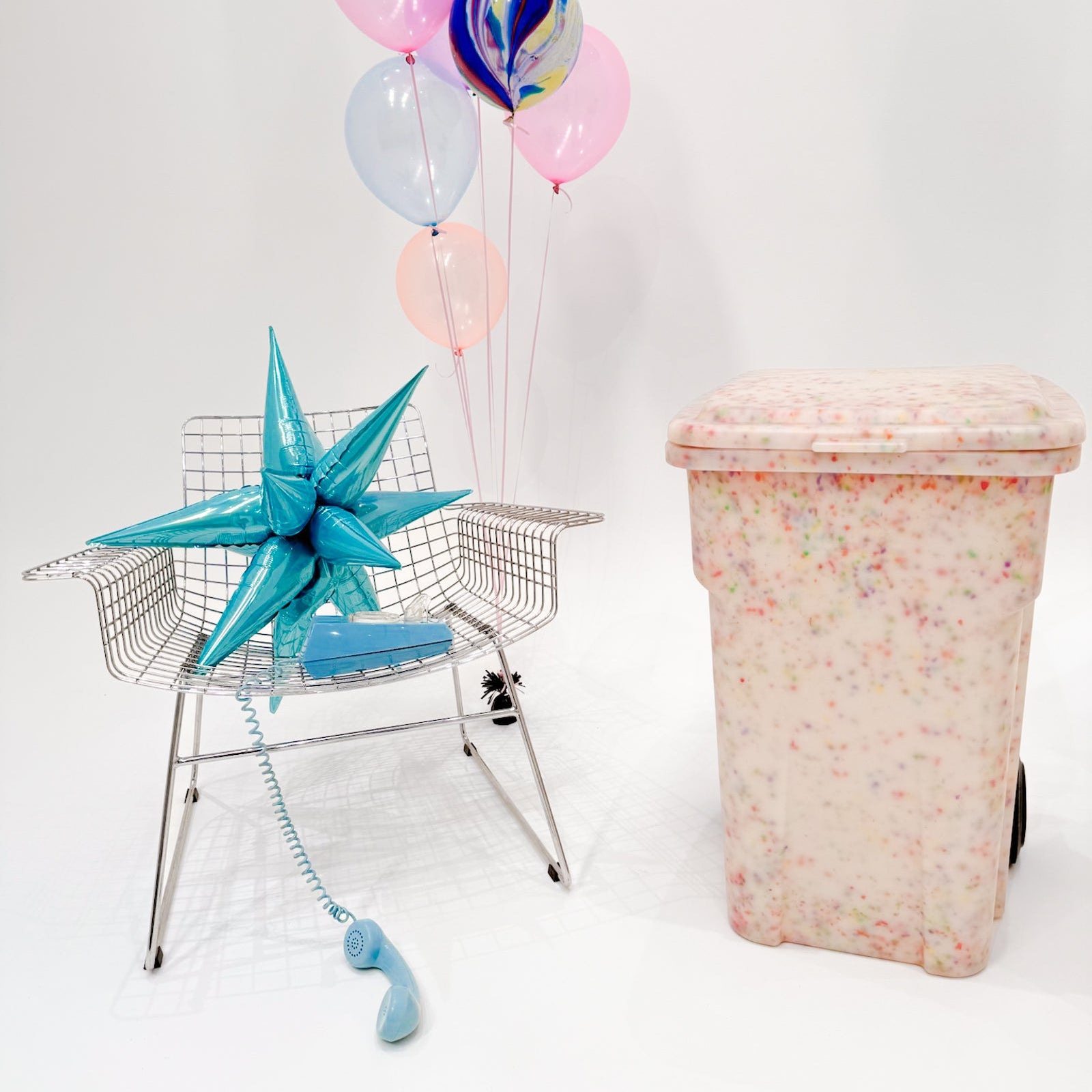 Decorative chair with balloons and a starfish next to a colorful trash can on a white background