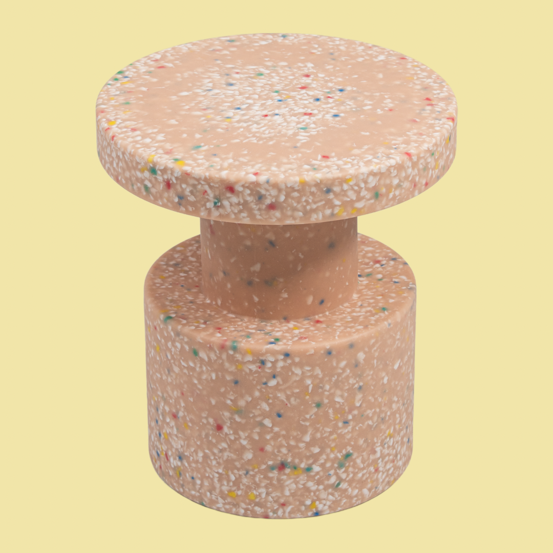 Round, multicolored concrete stool on a light yellow background