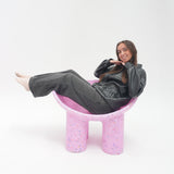 Person sitting on a pink chair with a white background