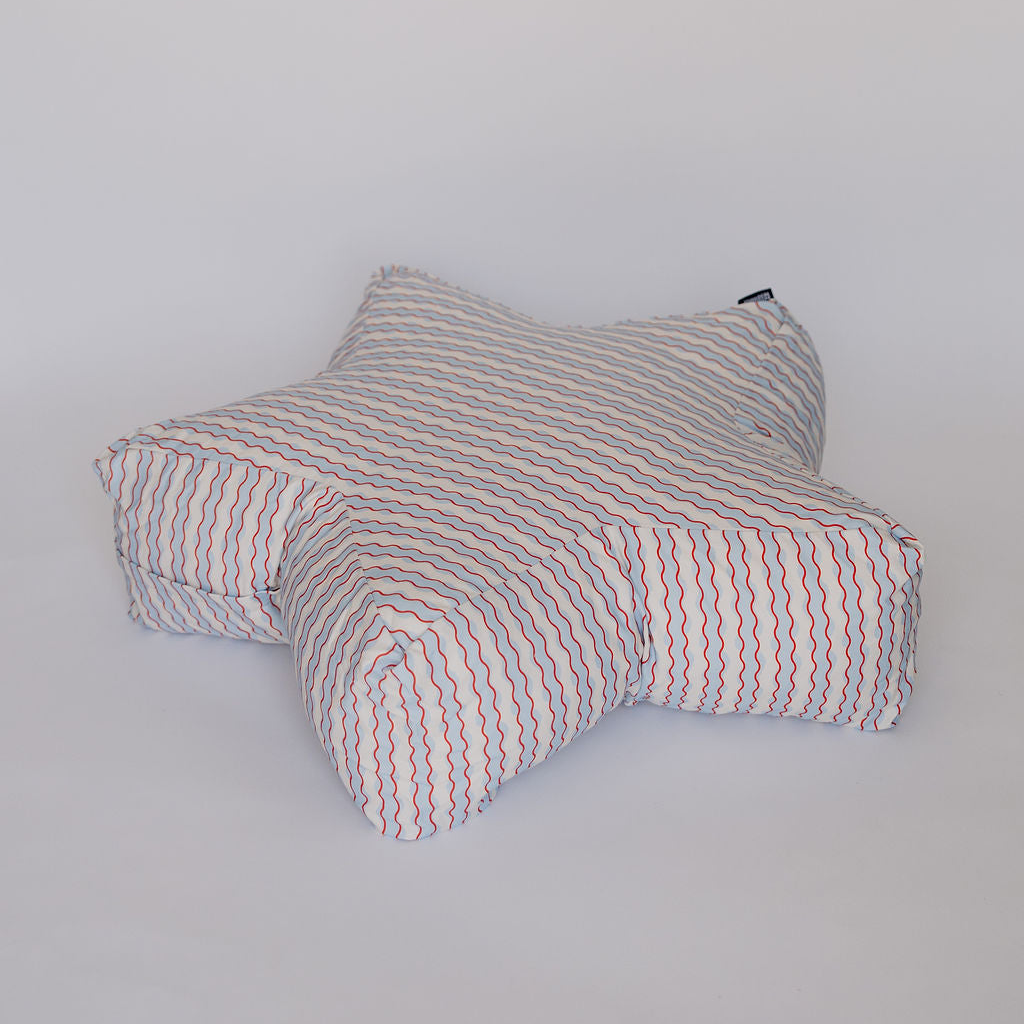 A star-shaped floor cushion with a white base and thin red and blue wavy stripes, photographed against a plain light gray background.